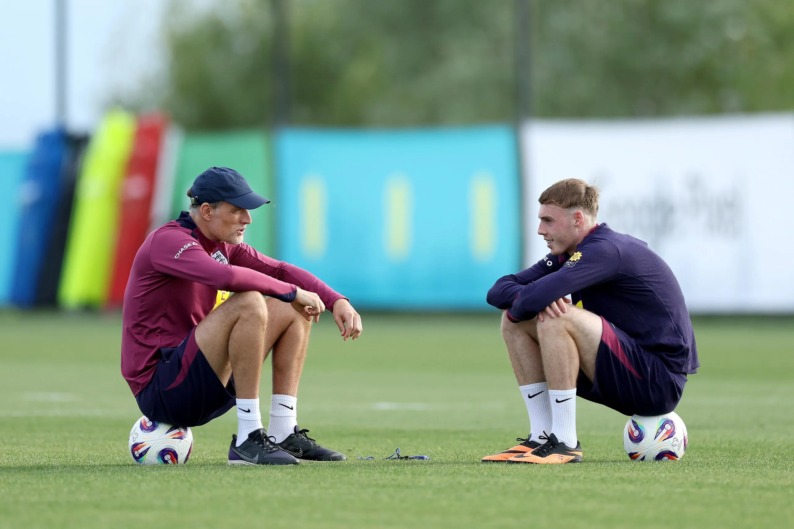 Thomas Tuchel and Cole Palmer sit on footballs at England training in Girona in 2025